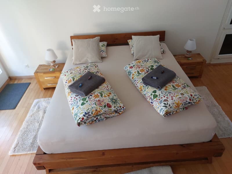Cozy bedroom with a wooden bed frame, floral-patterned duvet, matching pillows, and two nightstands with lamps.
