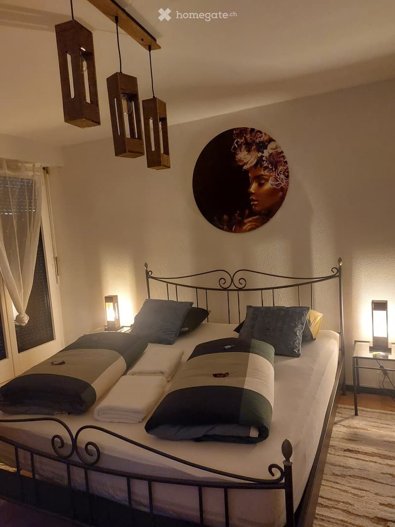 Cozy bedroom with a metal-framed bed, multiple pillows, a patterned blanket, nightstands with lamps, and a large circular wall art piece.