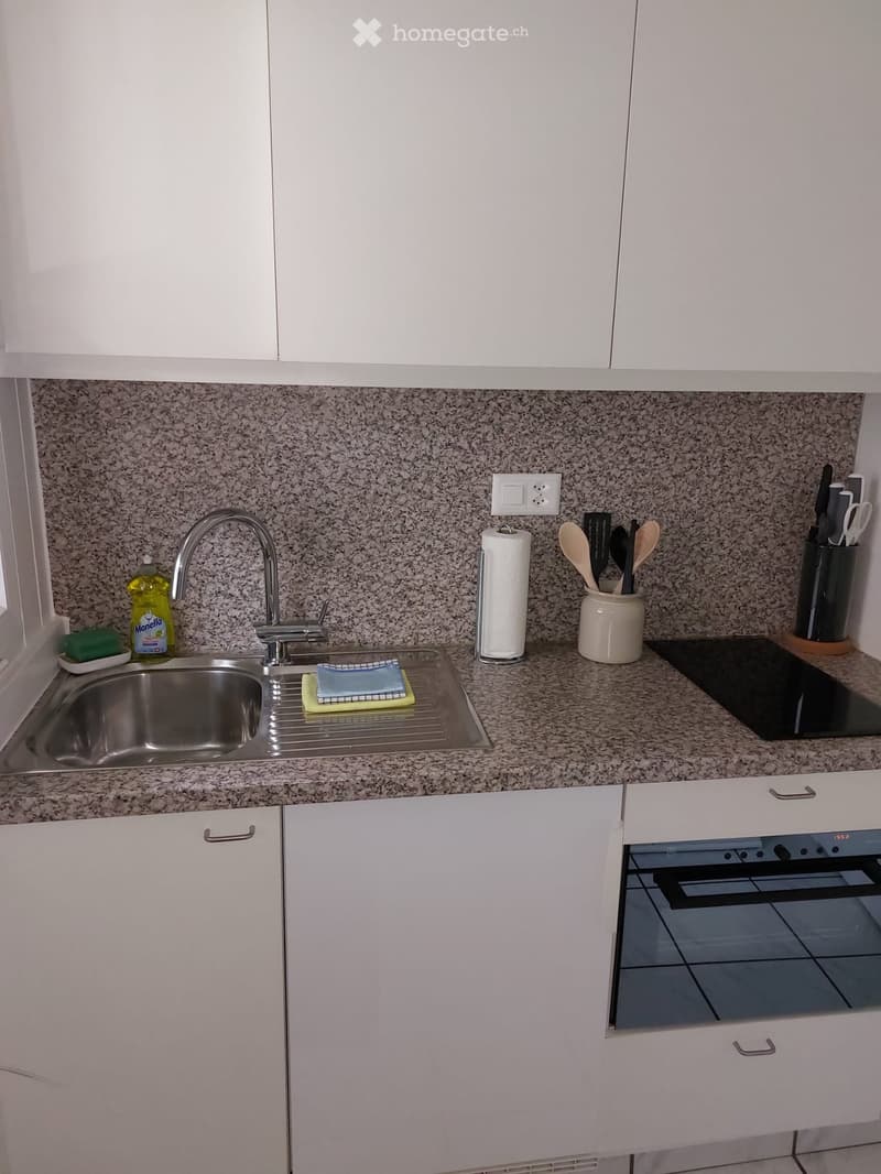 Modern kitchen with white cabinets, granite countertop, stainless steel sink, and various kitchen utensils including a knife block and spoon holder.