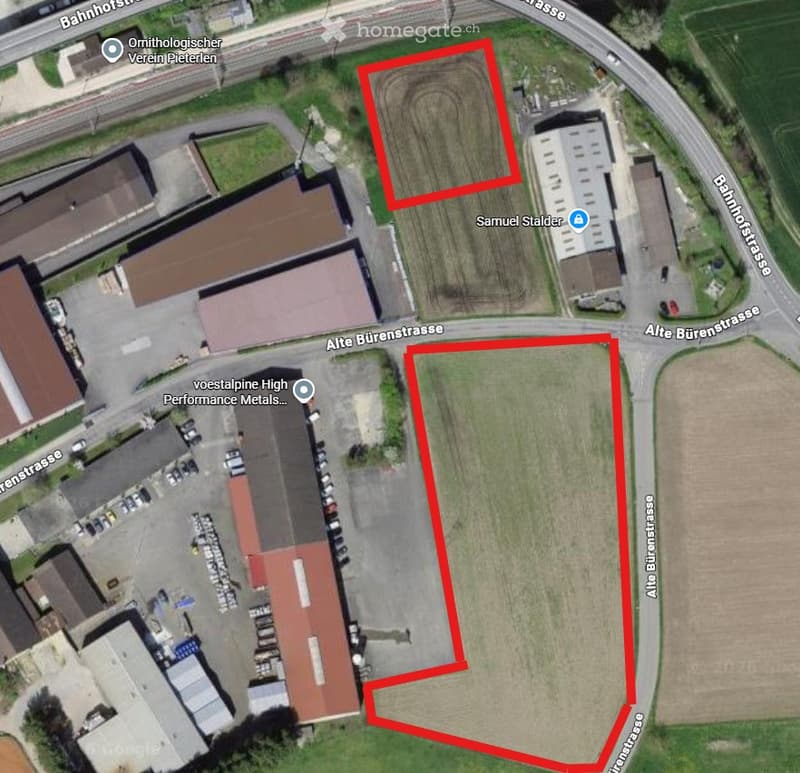 Aerial view of an industrial area with multiple buildings, parking lots, and surrounding roads. Red outlines highlight two plots of land.