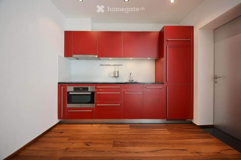 Modern kitchen with red cabinets, stainless steel oven, and wooden flooring.