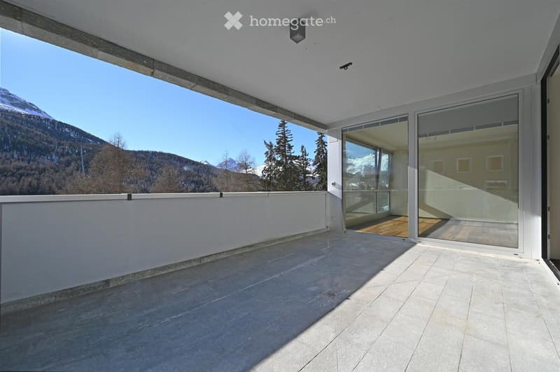 Modern balcony with large glass doors leading to an indoor space, expansive mountain view, and clean tiled flooring.