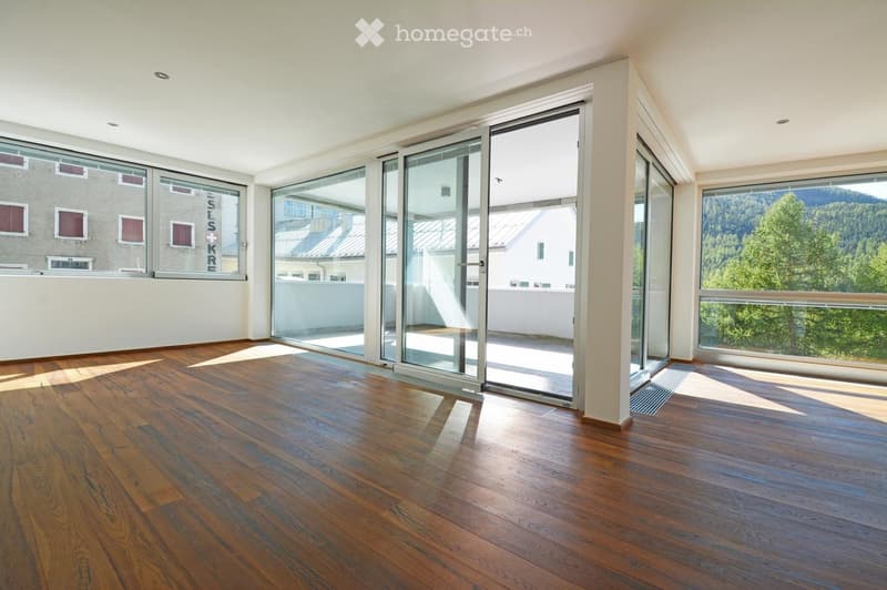 Empty room with wooden flooring, large windows, and sliding glass doors leading to a balcony.