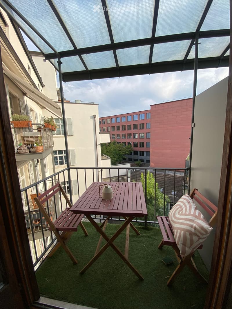 Balcony with artificial grass, wooden table, two chairs, and a decorative teapot.