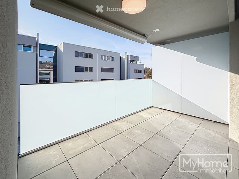 Modern balcony with tiled floor, white glass railing, and contemporary lighting fixture.