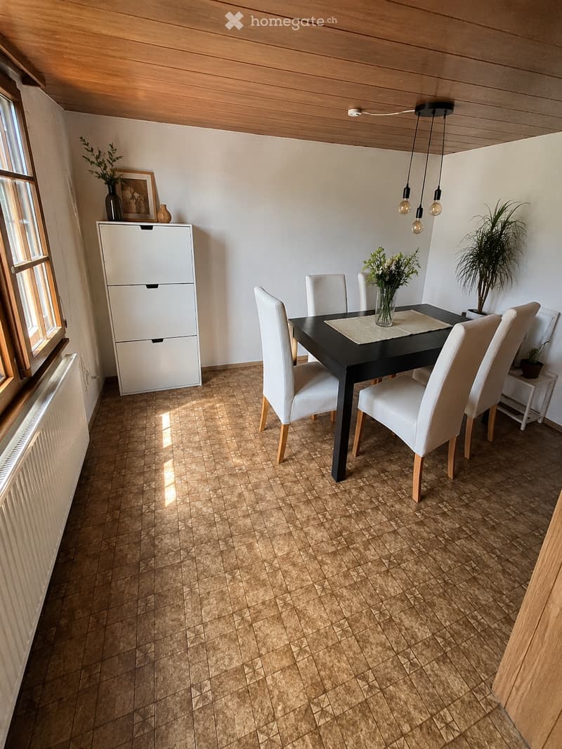 Dining room with a black dining table surrounded by white chairs, a white cabinet, and decorative vases on the windowsill.