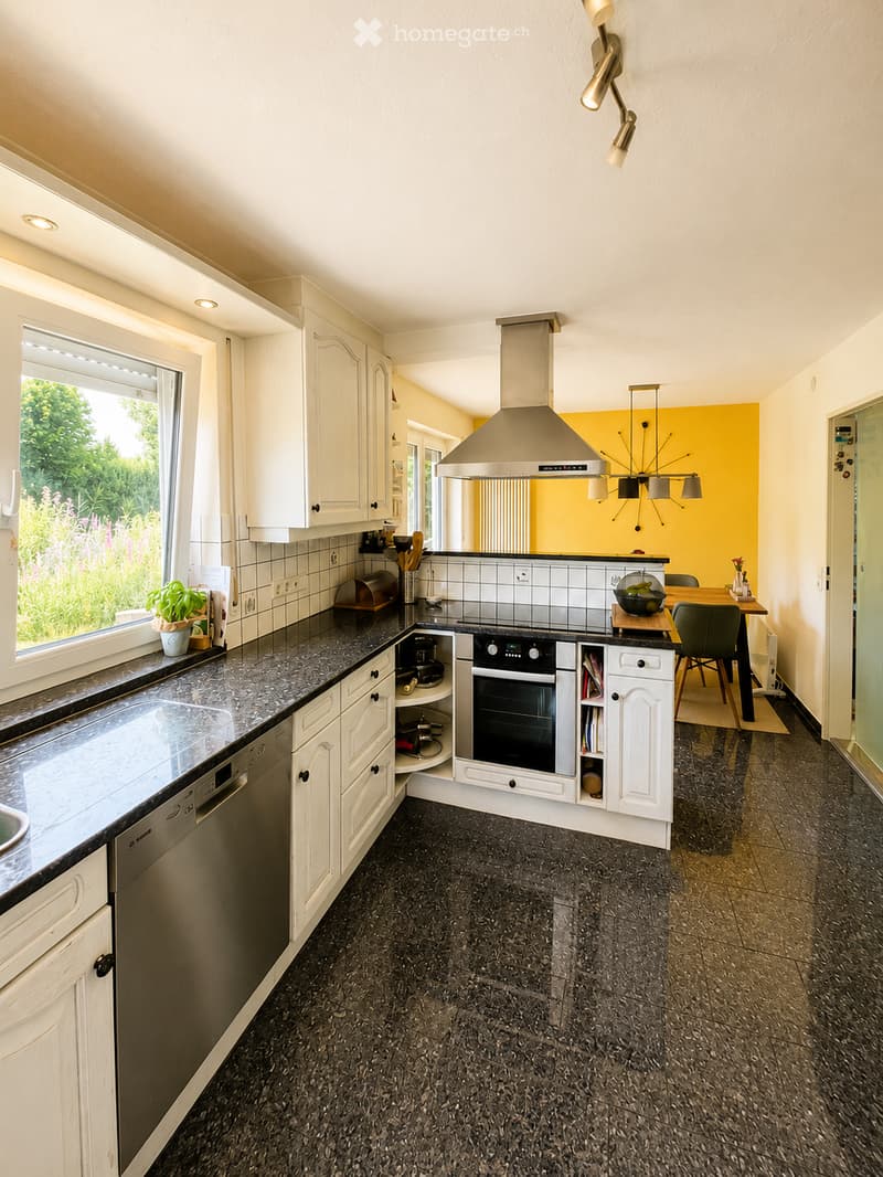 Modern kitchen with white cabinets, granite countertops, stainless steel appliances, and a central island. Features include a built-in oven, dishwasher, and a dining area with a table and chairs.