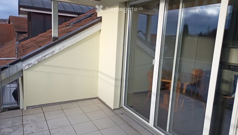 Balcony with tiled floor, large glass sliding doors, and a view of neighboring rooftops.