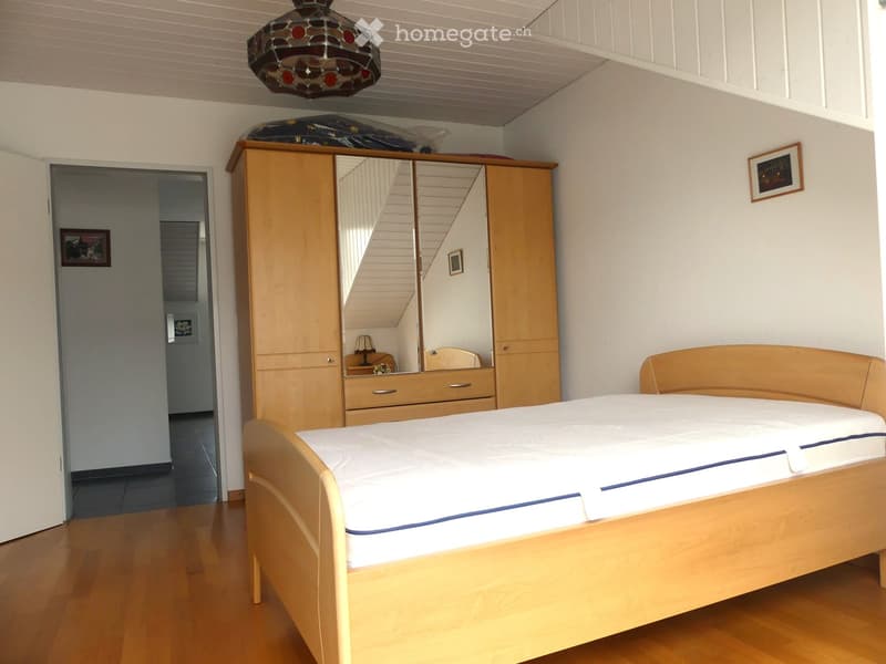 Bright bedroom with wooden bed, wardrobe with mirror, and a hanging stained-glass lamp.