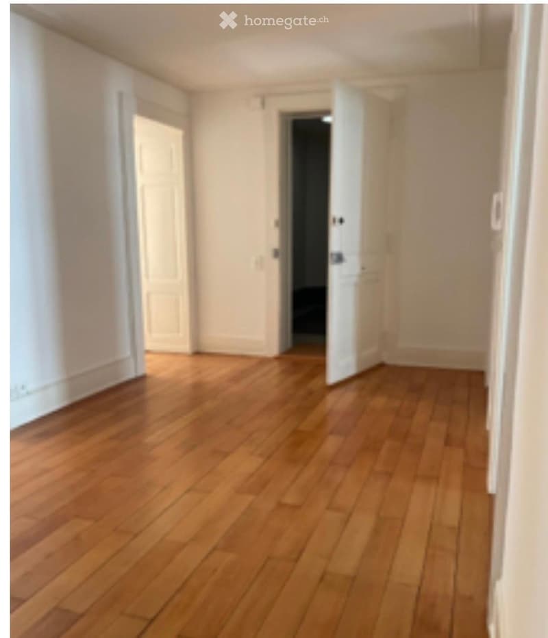 Empty hallway with wooden flooring and white walls, featuring two open doors leading to other rooms.