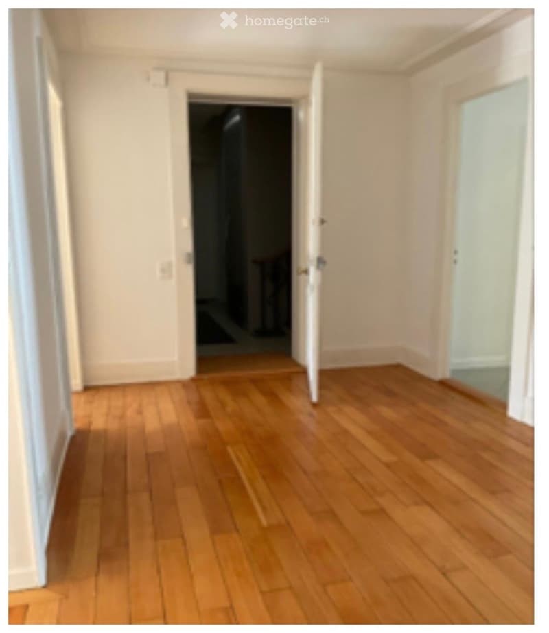 Empty hallway with wooden flooring and white walls, featuring open doors leading to other rooms.