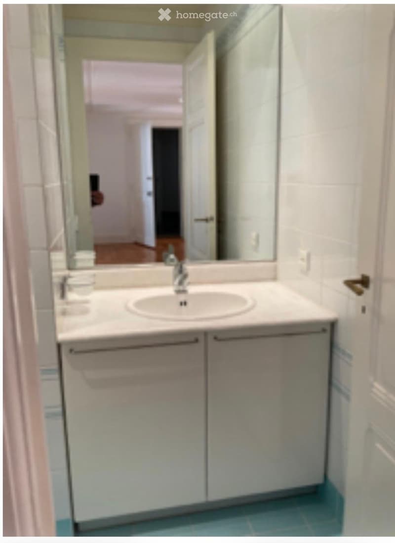 Bathroom with a white sink, mirror, and cabinets, featuring light blue tiled flooring.