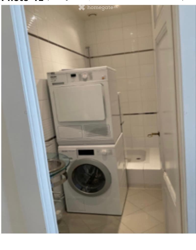 A small bathroom with a washing machine and dryer stacked, a bathtub, and tiled walls and floor.