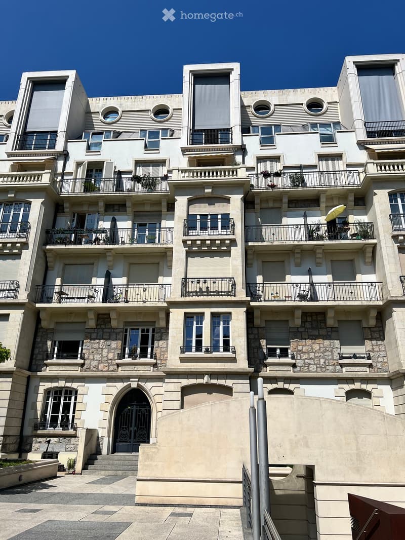 A multi-story residential building with balconies, large windows, and decorative stonework. Features include multiple balconies with railings, round windows, and a central arched entrance.