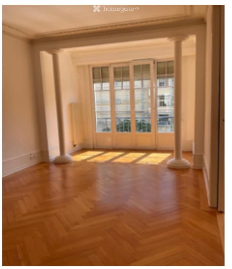 Empty room with wooden flooring, large windows, and white columns. No furniture or equipment present.
