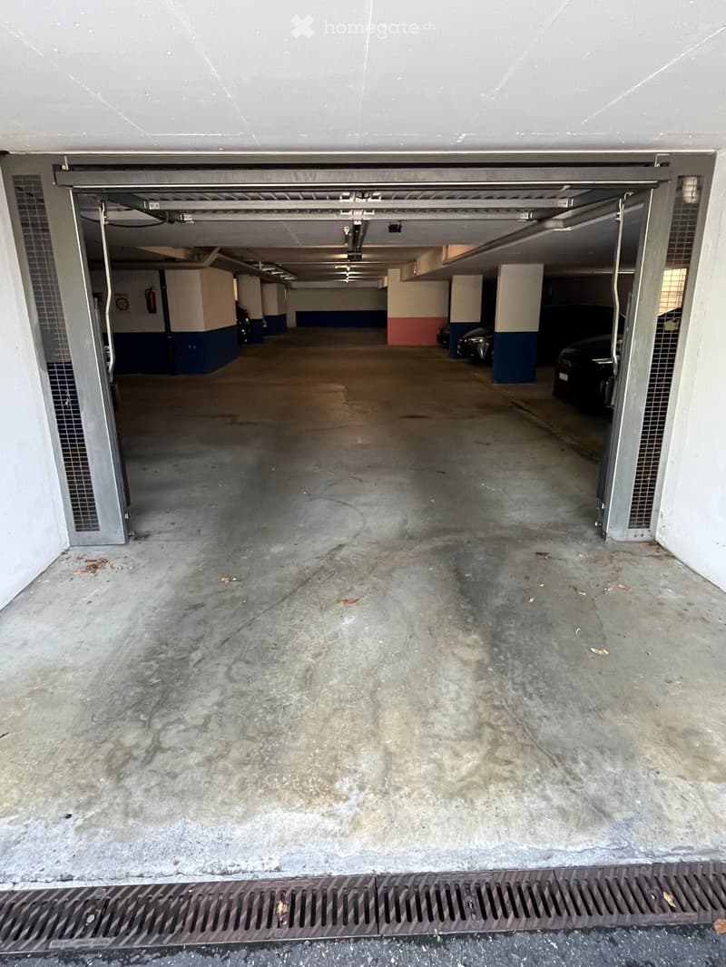 Underground parking area with concrete floors, pillars, and a few parked cars visible in the background.