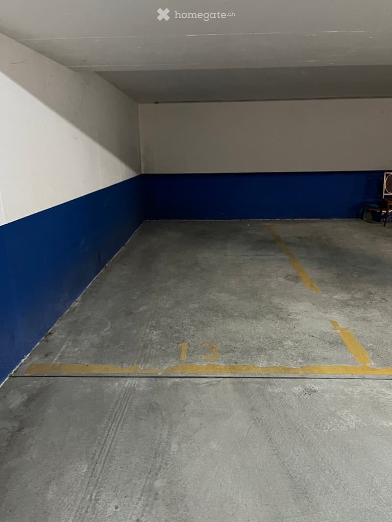 Empty parking space with concrete floor and blue-painted walls, marked with the number "13".
