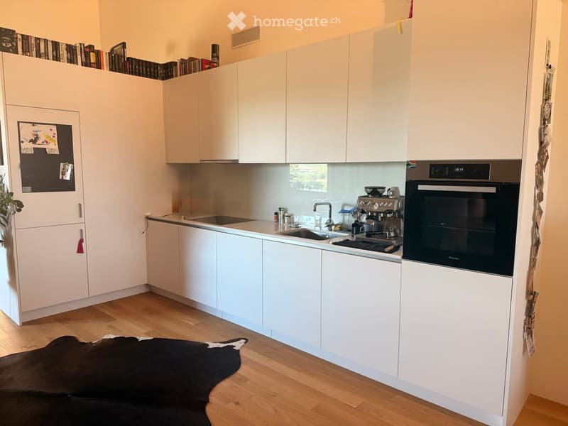 Modern kitchen with white cabinets, stainless steel appliances, a sink, coffee maker, and a black cowhide rug on the floor.