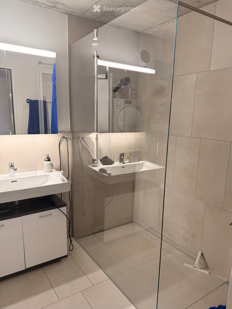 Modern bathroom with a white sink, mirrored cabinet, glass-enclosed shower, and beige tiled floor.