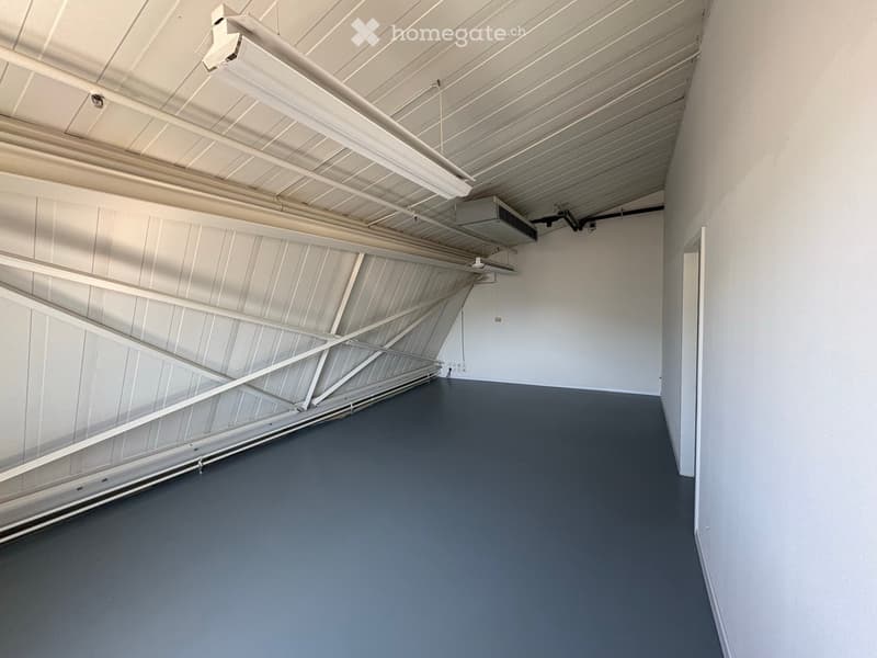 Empty room with grey flooring, white walls, and a metal-framed ceiling with exposed lighting fixtures and air conditioning units.