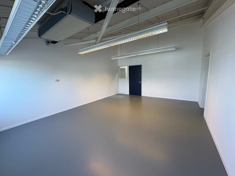 Empty room with white walls, grey floor, and fluorescent lighting fixtures. No furniture or equipment present.