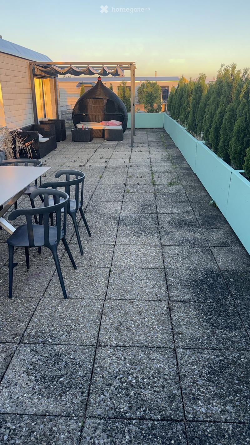 Rooftop terrace with a gravel surface, featuring a wicker bed, a table with chairs, and a small seating area with stools.