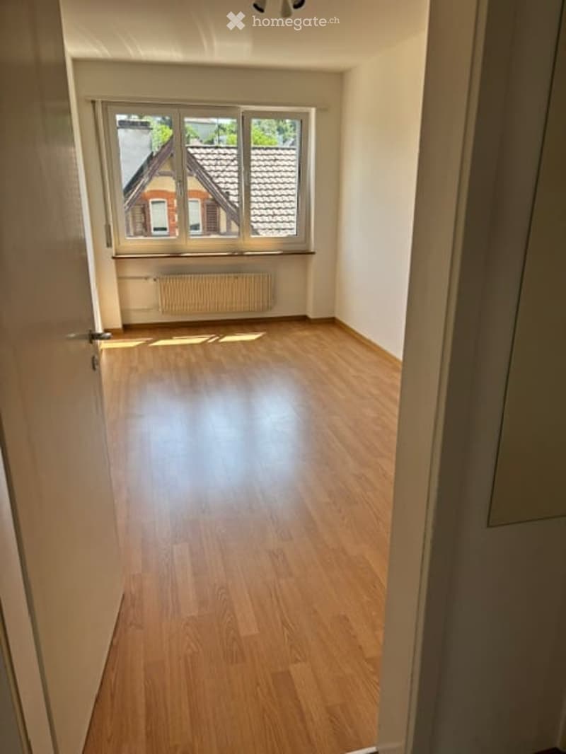 Empty room with wooden flooring, large window, radiator, and white walls.