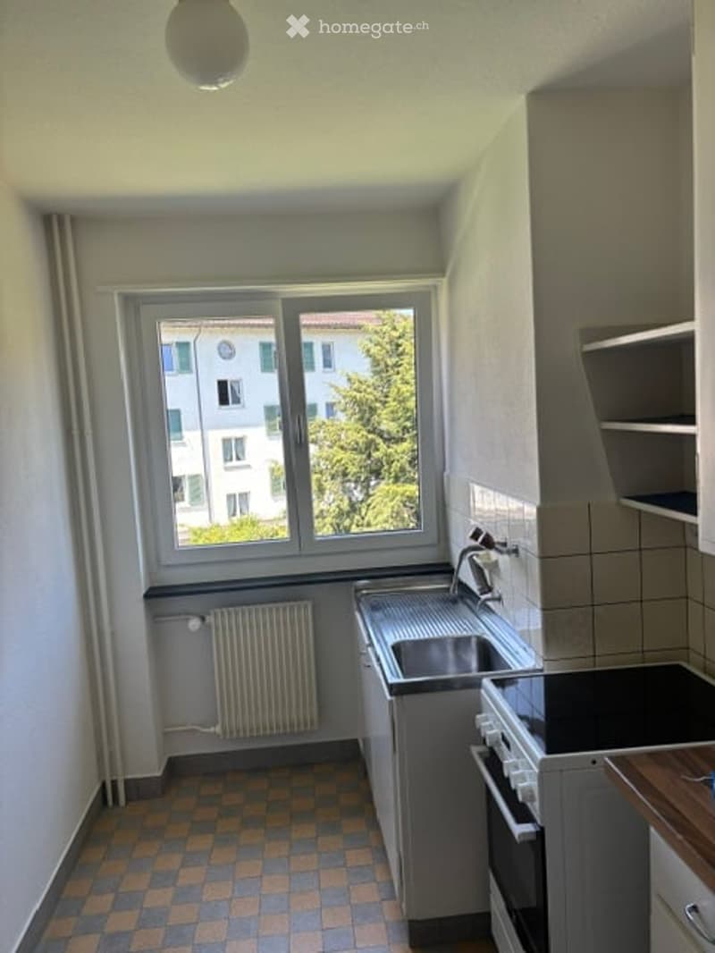 Empty kitchen with tiled floor, window, sink, and built-in cabinets.