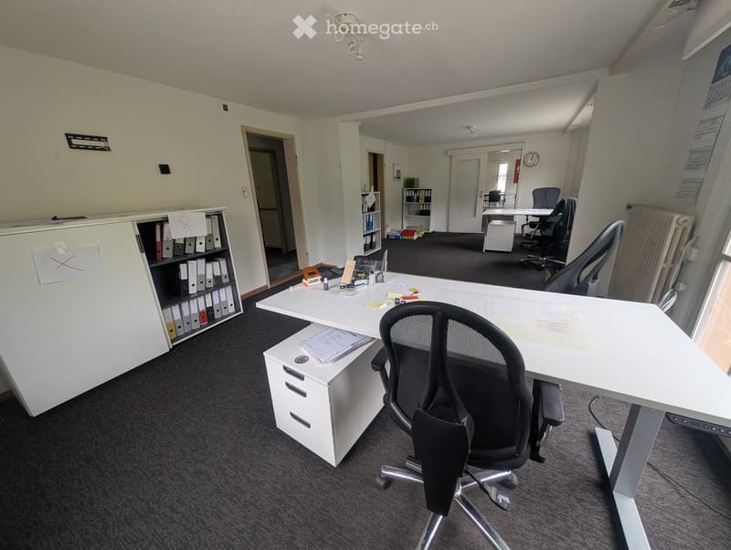 Office space with a large desk, ergonomic chair, filing cabinet, bookshelf, and additional workspace in the background.