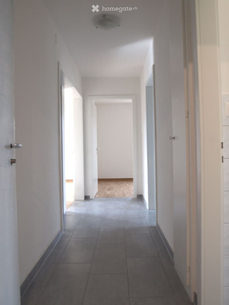 Empty hallway with tiled floor, white walls, and several doors leading to other rooms.