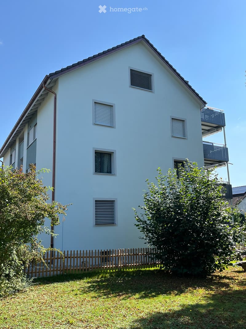 Two-story white house with multiple windows, a balcony, and a wooden fence in the front yard.
