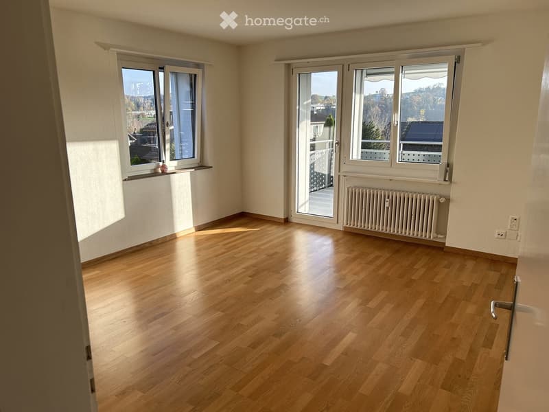Empty room with wooden flooring, large windows, radiator, and a small shelf on the windowsill.