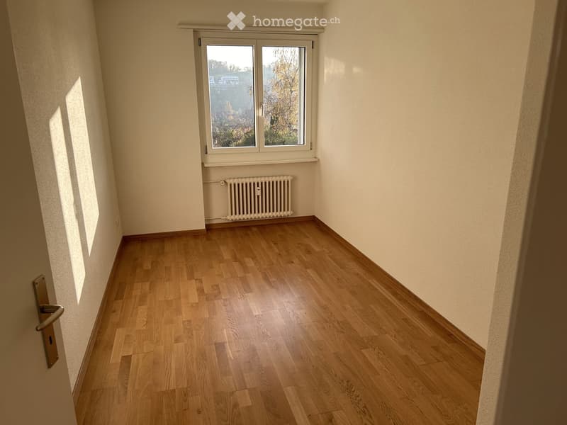 Empty room with wooden flooring, white walls, and a window with a radiator below it.
