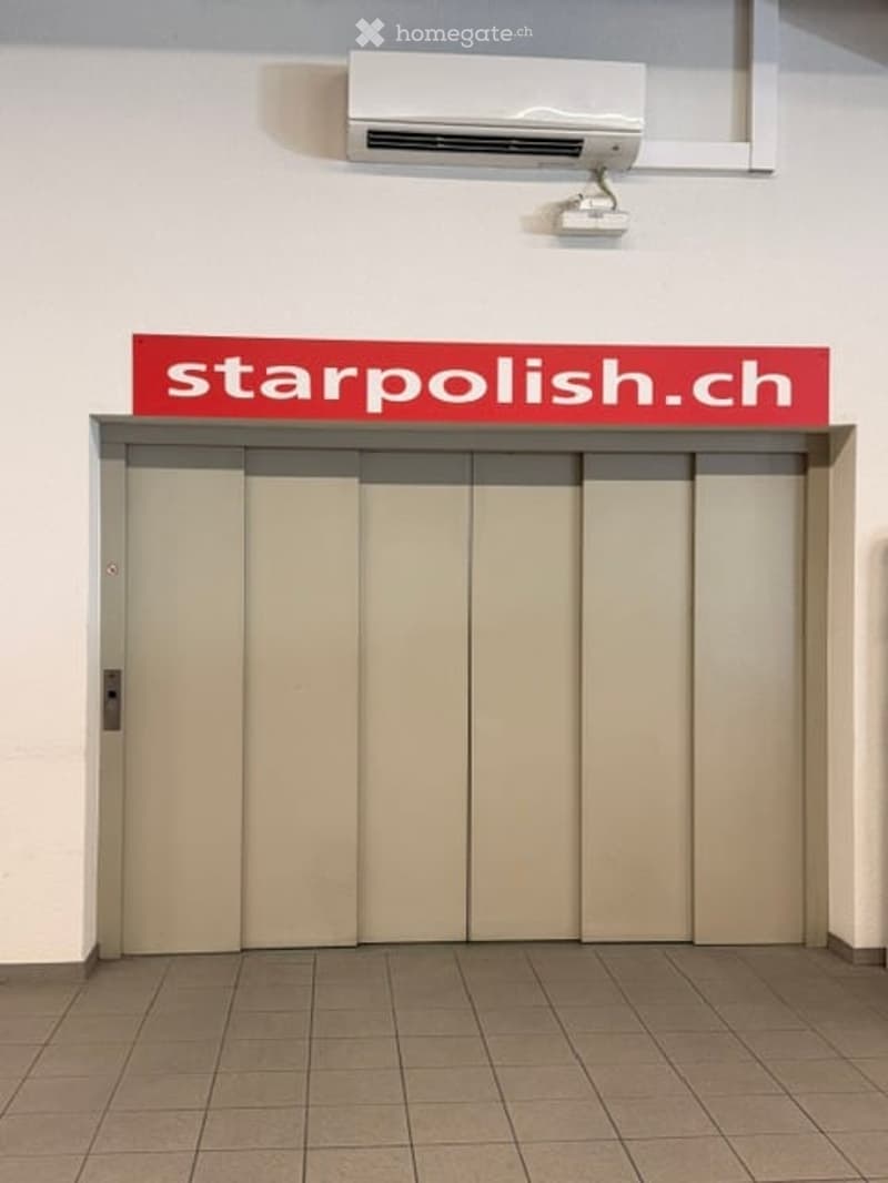Elevator entrance with a closed sliding door, a sign reading "starpolish.ch" above it, and an air conditioning unit mounted on the wall above.