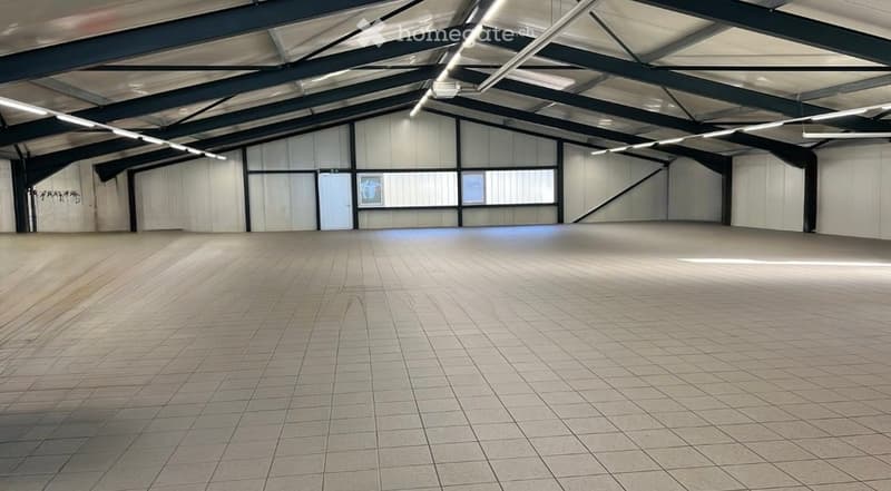 Empty industrial-style room with tiled floor, large windows, and exposed metal beams on the ceiling.