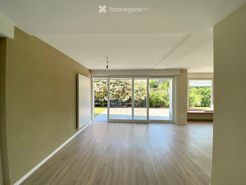 Empty room with wooden flooring, large sliding glass doors leading to an outdoor area, and a window on the right side.
