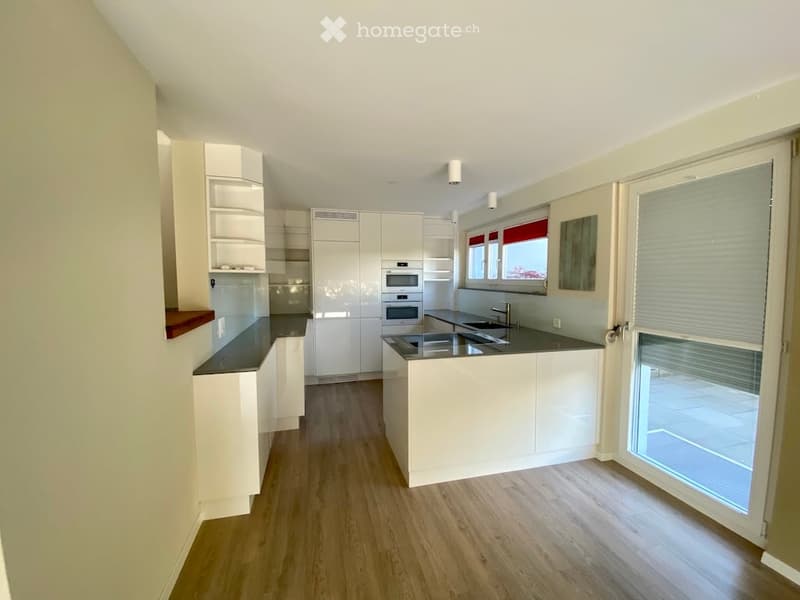 Modern kitchen with white cabinets, dark countertops, and a central island. Features include a sink, oven, and a large window with blinds offering a view.