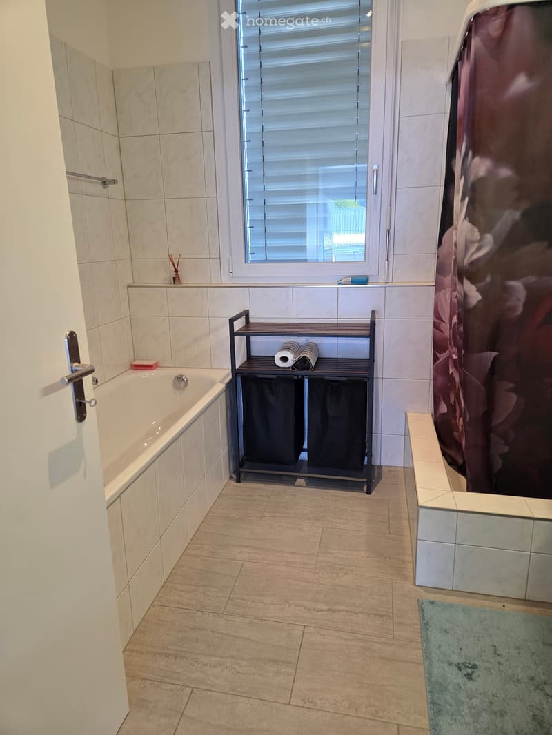 Modern bathroom with a bathtub, tiled walls, a window with blinds, a towel rack, and a shower curtain.