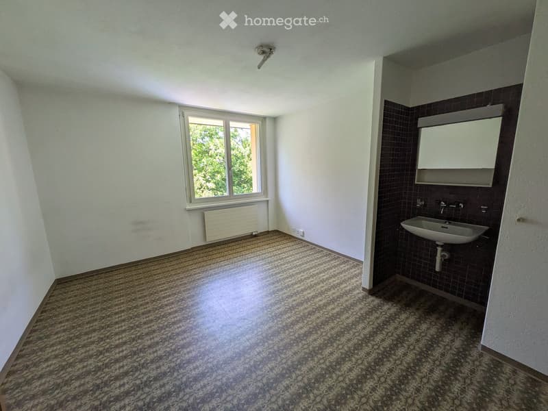 Empty room with white walls, granite flooring, a window with white frame, radiator, and a sink with mirror in the corner.