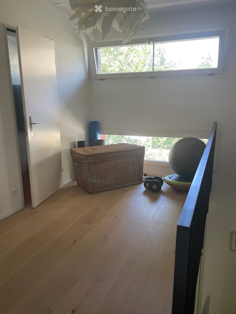 Bright hallway with wooden flooring, large window, wicker chest, decorative ball, and cushions near the window.
