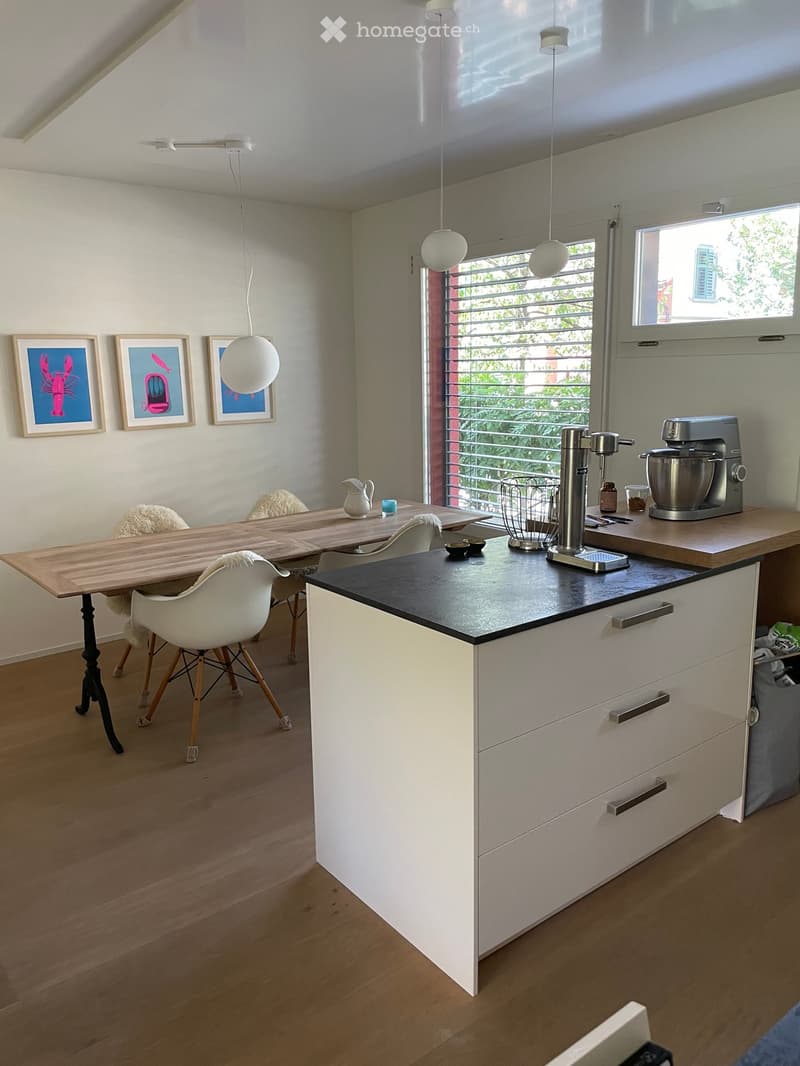 Modern kitchen with white cabinets, wooden table, white chairs, mixer, and framed pictures on the wall.