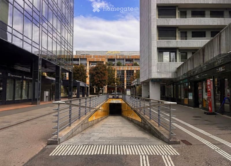 Modern urban area with raised ground floor, metal railings, and surrounding buildings.