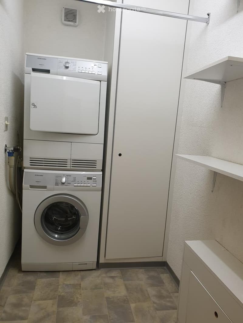 Bathroom with a stacked washing machine and dryer unit, white cabinets, and tiled floor.