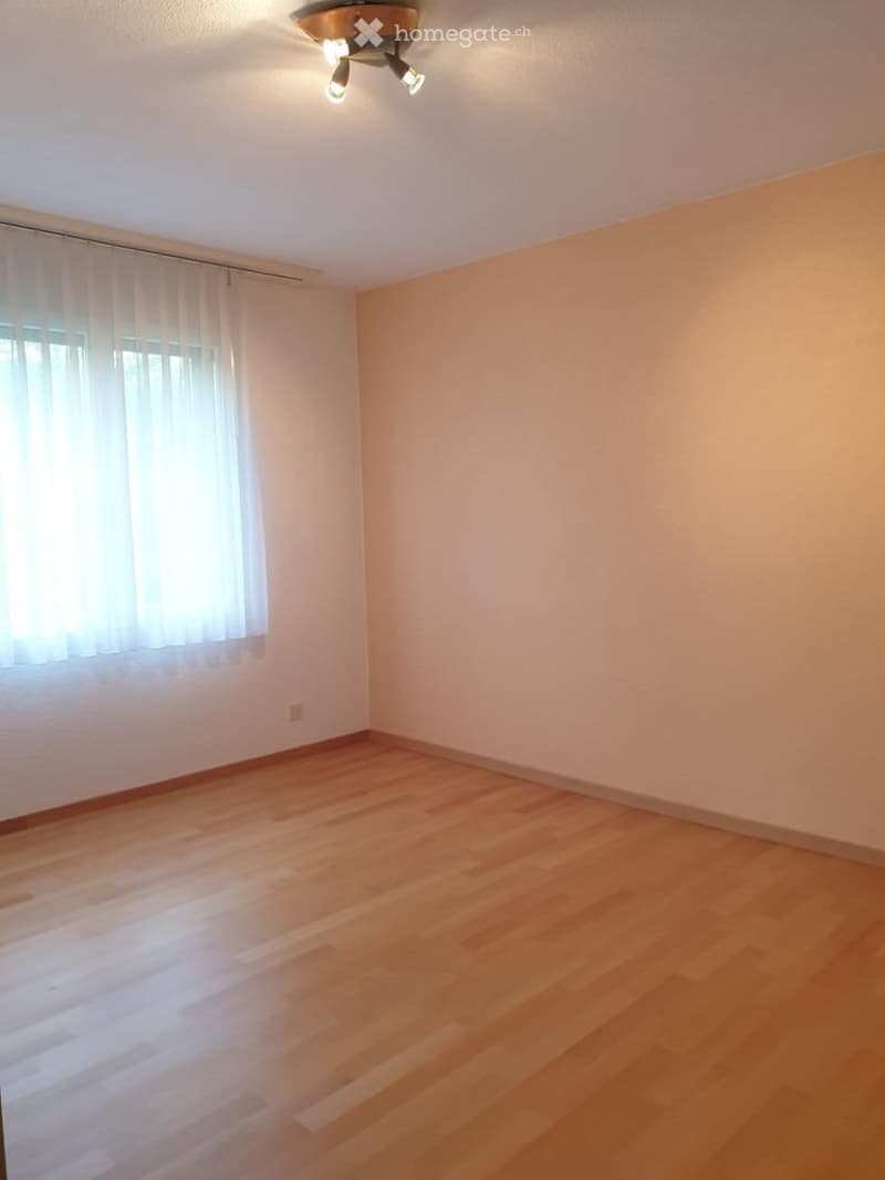 Empty room with wooden flooring, white walls, and a window with white curtains. No furniture or equipment is present.