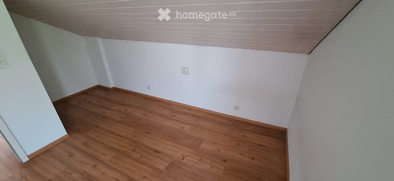 Empty room with wooden flooring and white walls, featuring a slanted ceiling and visible electrical outlets.