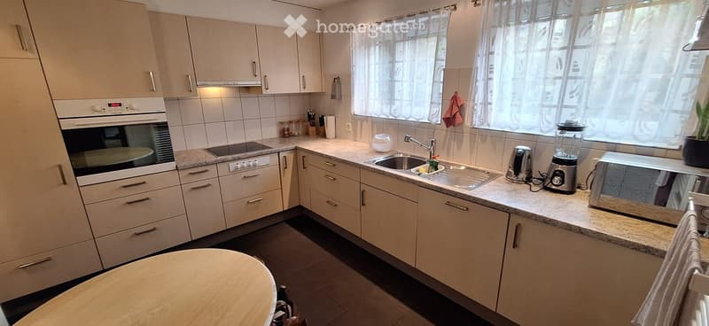 Modern kitchen with white cabinets, granite countertops, stainless steel appliances, and a small round wooden table.
