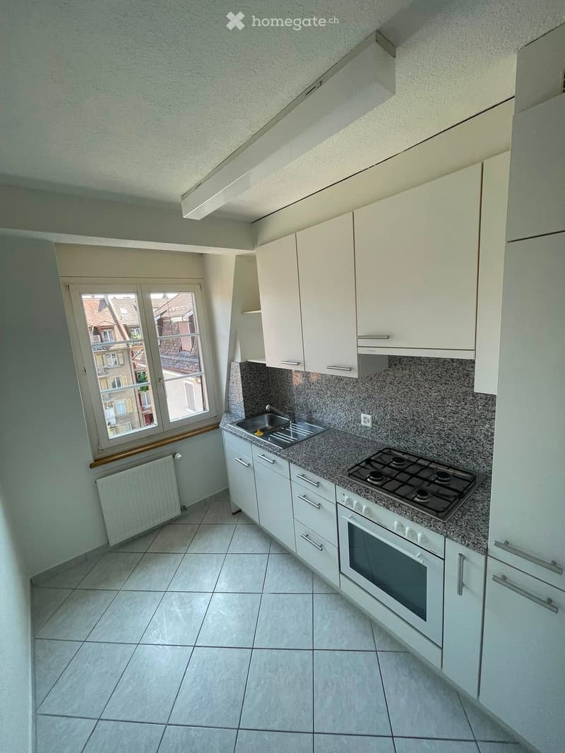 Modern kitchen with white cabinets, granite countertop, stainless steel sink, gas stove, and oven. Features a window with a view of rooftops.