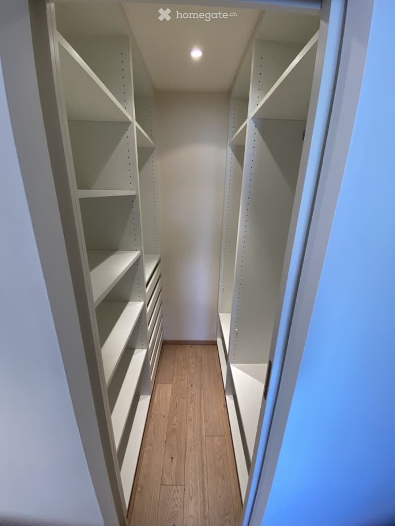 Empty closet with built-in white shelving units and wooden flooring.