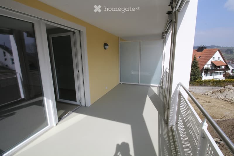 Balcony with large glass sliding doors, white railing, and a view of the surrounding area.