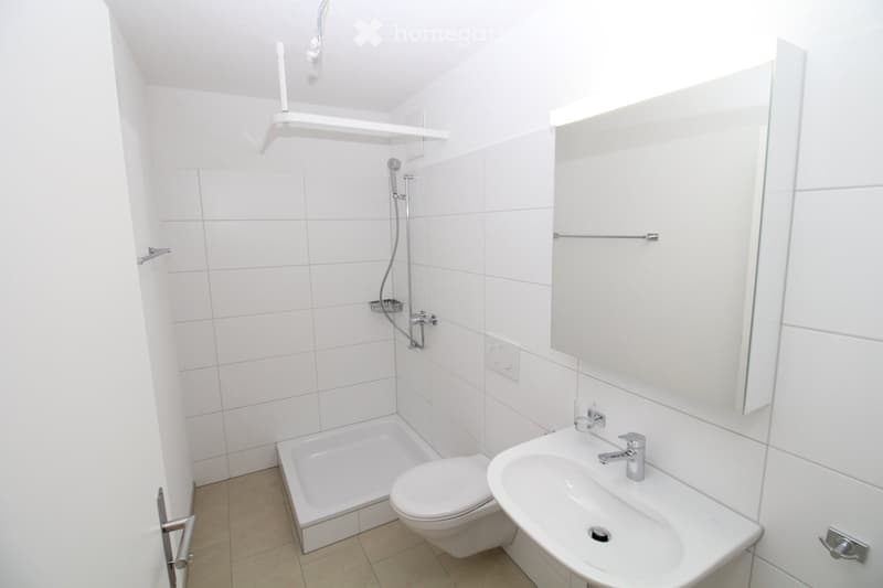 Modern bathroom with white tiles, a bathtub, toilet, sink, mirror, and a showerhead with a handheld sprayer.
